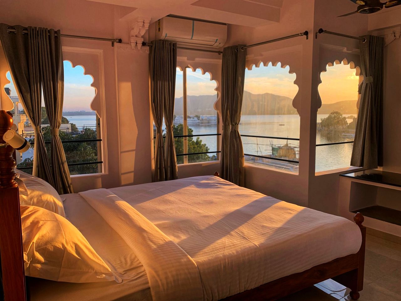 Sunlit bedroom with serene lake view through ornate windows at sunset.
